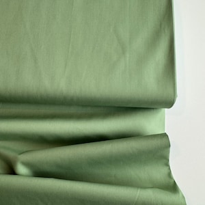 May include: A close-up of a folded piece of green fabric. The fabric has a smooth, even texture and a slightly sheen finish.