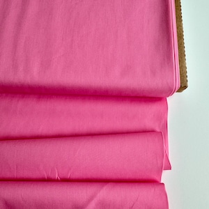 May include: A roll of pink cotton fabric folded in thirds. The fabric is smooth and has a slight sheen.