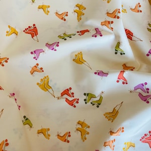 May include: Off-white fabric with a repeating pattern of colorful roller skates. The skates are in shades of orange, yellow, green, and purple, with brown laces and wheels. The fabric has a soft, flowing appearance.