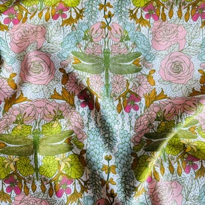 Peut inclure: Un tissu pr&eacute;sentant un motif r&eacute;p&eacute;titif de libellules vertes, de roses roses et de grappes florales bleu clair sur un fond blanc avec de petits points noirs. Le design inclut des feuilles et des tiges vert-jaune dispos&eacute;es sym&eacute;triquement.