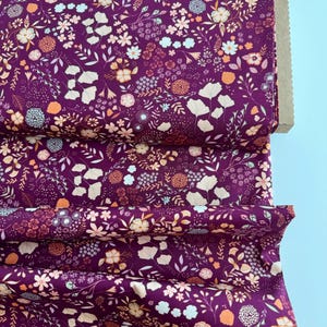 May include: Purple fabric with a small-scale floral print in shades of pink, orange, and white. The fabric is folded and has a brown cardboard backing.