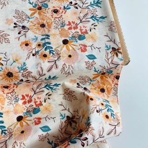 May include: White fabric with a floral pattern featuring orange, yellow, pink, and teal flowers. The fabric is folded and has a brown cardboard backing.