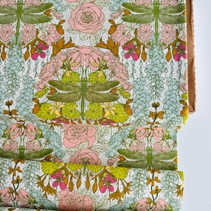 Peut inclure: Un rouleau de tissu pr&eacute;sentant un motif r&eacute;p&eacute;titif de libellules vertes, de roses roses et de grappes de fleurs bleu clair sur un fond blanc. Le design comprend des lignes complexes et des &eacute;l&eacute;ments botaniques vibrants dispos&eacute;s sym&eacute;triquement.