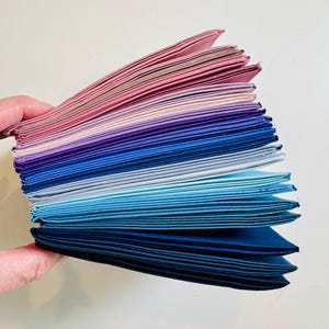 May include: A stack of fabric squares in shades of pink, purple, blue, and teal. The fabric is folded neatly and arranged in a gradient pattern.