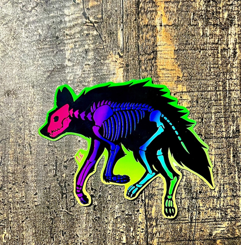 May include: A holographic sticker featuring a stylized hyena with a skeleton design. The hyena's skull is pink, the rib cage is purple and blue, and the outline is neon green. The sticker is on a wooden surface.