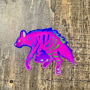 May include: A vibrant sticker featuring a stylized hyena in shades of pink, blue, and green. The hyena has striped markings and is depicted in a walking pose. The sticker is on a wooden surface.