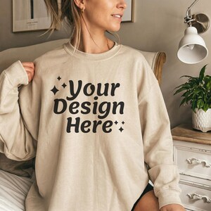 May include: A beige sweatshirt featuring the text "Your Design Here" in a bold, black font. The text is centrally placed on the front of the long-sleeved, crew neck top. The sweatshirt has a relaxed fit.