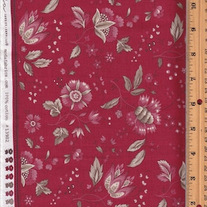 May include: Red fabric with a floral pattern featuring large, stylized flowers in shades of pink and taupe, along with smaller blossoms and leaves. The fabric has a border with text that reads "moda fabrics".
