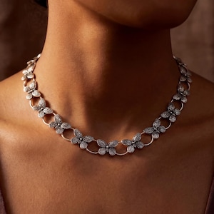 May include: A silver necklace with a repeating pattern of butterfly pendants. The necklace is worn around the neck, displaying the detailed design and metallic sheen. The butterflies are connected by circular links, creating a delicate chain.