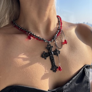 May include: A black metal cross pendant necklace with red glass beads and chain accents.