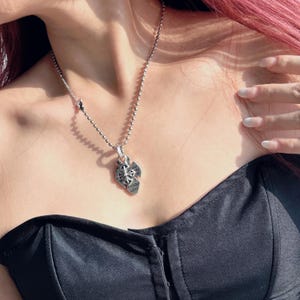 May include: A silver chain necklace with a pendant featuring a multi-layered heart design with intricate details and engraved text.