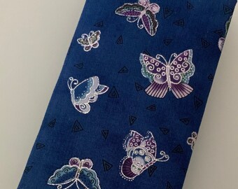 Può includere: Un portafoglio in tessuto blu con un motivo di farfalle e triangoli. Le farfalle sono in tonalità di viola, verde e bianco.