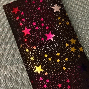 May include: A black fabric pouch with a gradient of pink, yellow, and gold stars on a black background.