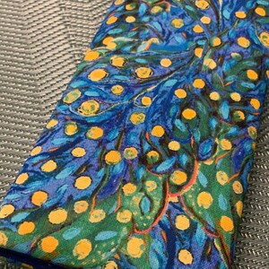 Könnte beinhalten: Eine lange, rechteckige blaue Stofftasche mit einem wirbelnden Muster aus Gelb, Grün und Blau. Der Stoff hat eine strukturierte, fast marmorierte Optik.