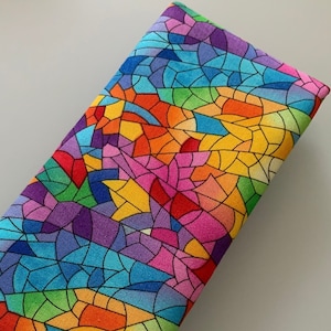 May include: A long, rectangular clutch purse with a colorful stained glass pattern. The pattern features a variety of colors, including red, orange, yellow, green, blue, purple, and pink.