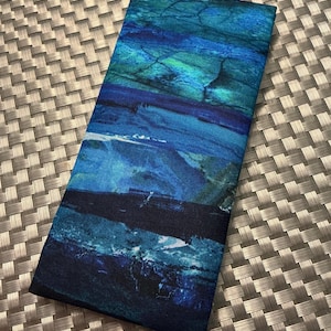 May include: A rectangular fabric case featuring a vibrant abstract print with horizontal bands of deep navy, royal blue, turquoise, and teal. The surface displays a textured, marbled pattern with dark crackle lines throughout the blue color palette.