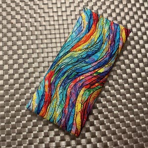 May include: A rectangular fabric pouch featuring a vibrant, multi-colored abstract pattern with flowing, wavy lines in shades of red, orange, yellow, green, blue, and purple. The design has a textured, watercolor-like appearance throughout.