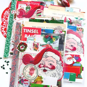 May include: A collection of vintage-style Christmas paper ephemera including die-cut Santa Claus figures, book pages titled The Silver Skates, Shiny Brite labels, gift tags, and decorative holiday stickers arranged in a layered stack.