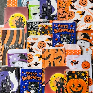 Pu&ograve; includere: Una collezione di sacchetti di carta a tema Halloween con vari disegni, tra cui zucche, fantasmi, pipistrelli e gatti. I sacchetti riportano il testo "Happy Halloween" e "Trick or Treat".