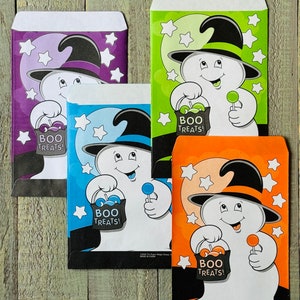 Pu&ograve; includere: Quattro sacchetti di dolcetti di Halloween con un fantasma che indossa un cappello da strega che tiene un lecca-lecca e una borsa che dice "Boo Treats!" I sacchetti sono viola, verde, blu e arancio.