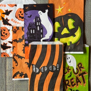 Pu&ograve; includere: Cinque sacchetti di carta a tema Halloween con diversi design. Un sacchetto presenta un fantasma e una casa stregata, un altro ha una zucca intagliata, uno ha un motivo a righe con la parola "Boo!" su di esso, uno ha pipistrelli e zucche, e l'ultimo ha un fantasma e le parole "Trick or Treat".