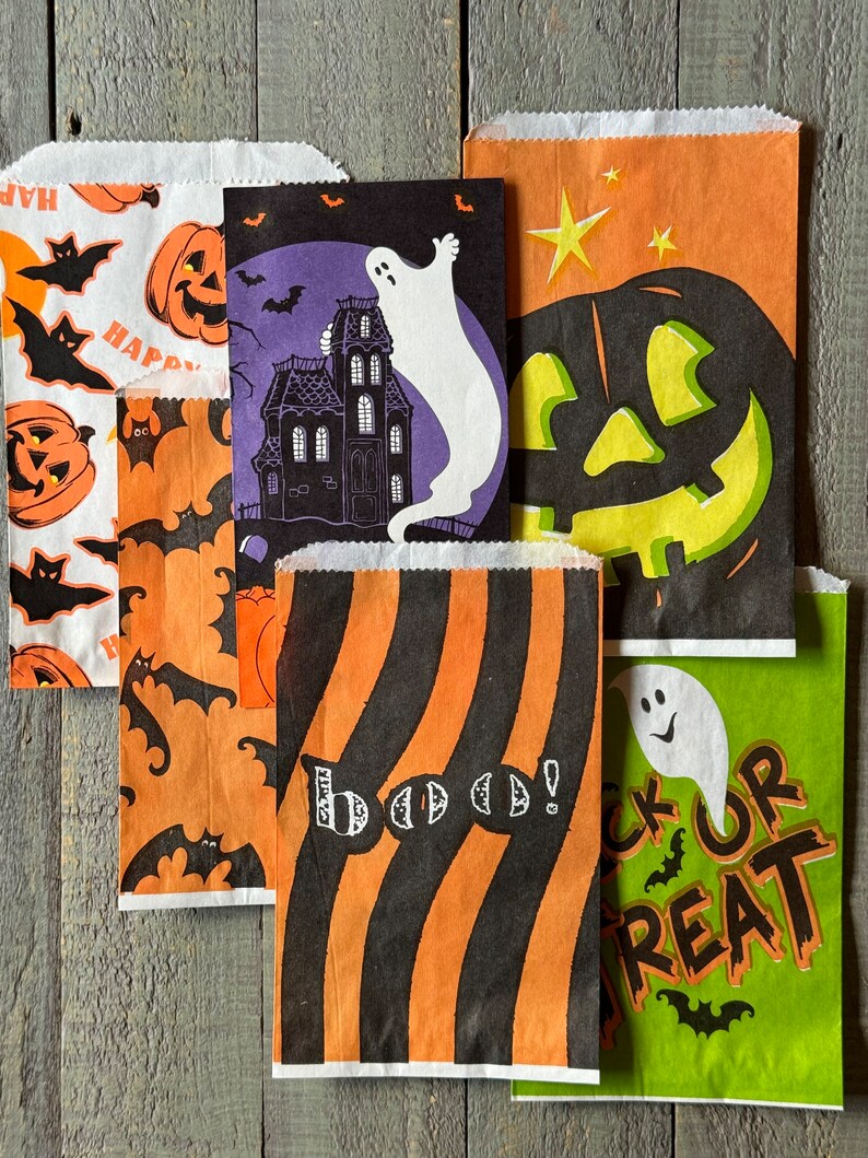 Pu&ograve; includere: Cinque sacchetti di carta a tema Halloween con diversi design. Un sacchetto presenta un fantasma e una casa stregata, un altro ha una zucca intagliata, uno ha un motivo a righe con la parola "Boo!" su di esso, uno ha pipistrelli e zucche, e l'ultimo ha un fantasma e le parole "Trick or Treat".