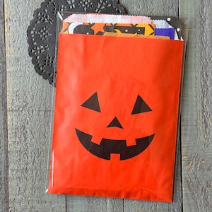 Pu&ograve; includere: Un sacchetto di carta rosso con una faccia di zucca nera stampata su di esso. Il sacchetto &egrave; pieno di ritagli di carta colorati e con motivi.