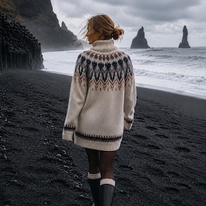 Könnte beinhalten: Ein cremefarbener Rollkragenpullover mit einem dunkelbraunen, grauen und rostfarbenen geometrischen Muster an der Passe und am Saum. Der Pullover hat lange Ärmel sowie gerippte Bündchen an Kragen, Ärmeln und Saum und wird mit schwarzen Gummistiefeln getragen.