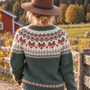 Peut inclure: Un pull en tricot à manches longues avec une base vert foncé et un empiècement crème orné d'un motif répétitif de visages de renards orange et marron, de formes géométriques et un chapeau fedora en feutre marron avec une bande tressée.