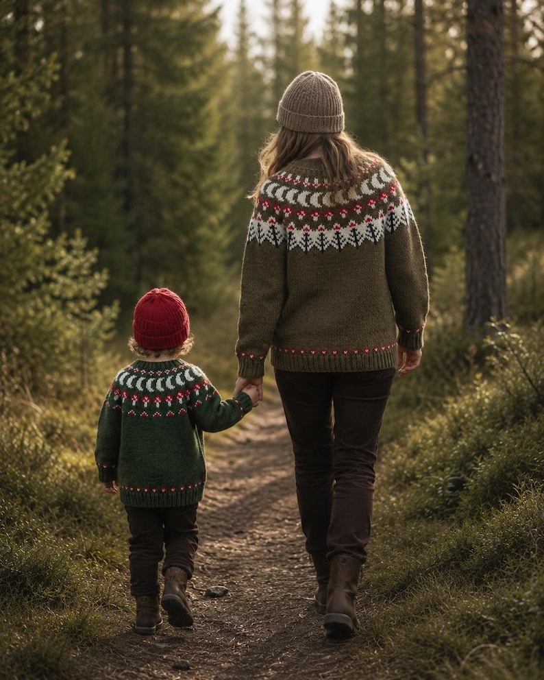 May include: Two individuals wearing matching olive green knit sweaters with a white and red patterned yoke featuring crescent moons and mushroom motifs. The taller individual wears a tan beanie and dark pants, while the smaller wears a red beanie.