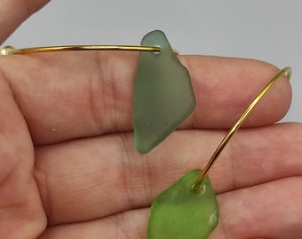 Pode incluir: Um bracelete de ouro com duas peças de vidro do mar presas. O vidro do mar é verde e verde claro.