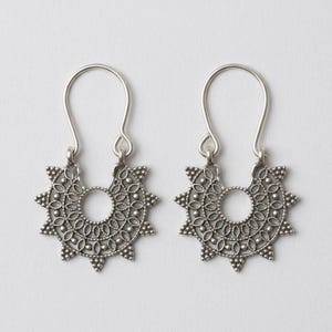 Può includere: Un paio di orecchini in metallo color argento con un design semicircolare ispirato ai raggi solari, caratterizzati da intricati intagli in filigrana, piccoli dettagli a perline lungo i bordi e un gancio curvo per l'orecchio.