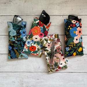 May include: Four floral print eyeglass cases in various colors, including black, white, and cream. Each case holds a pair of glasses or sunglasses. The cases feature a variety of colorful floral patterns, with glasses visible in some cases.