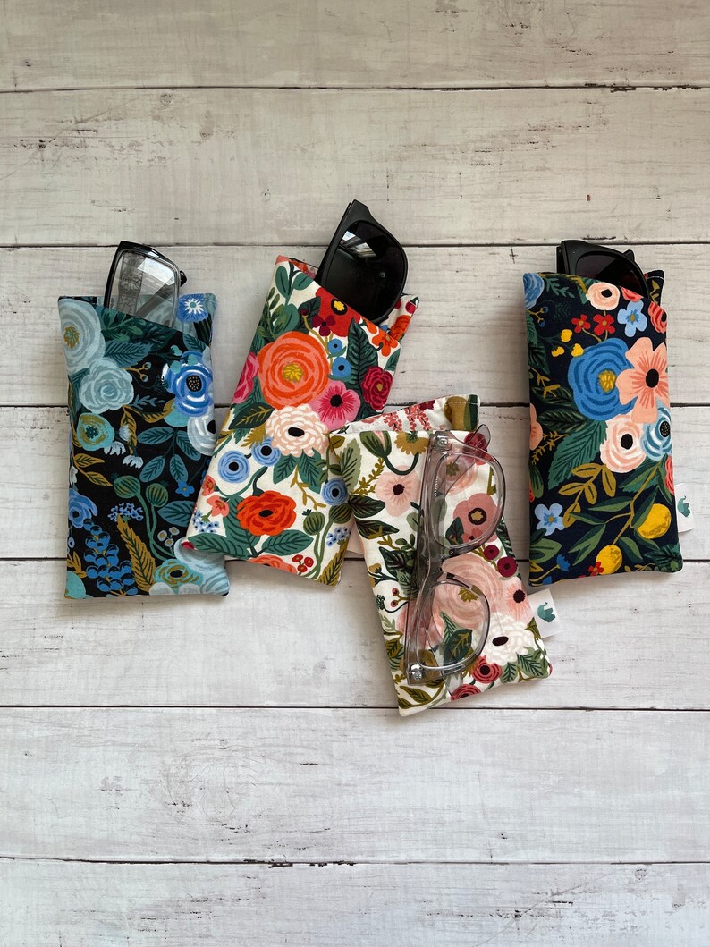 May include: Four floral print eyeglass cases in various colors, including black, white, and cream. Each case holds a pair of glasses or sunglasses. The cases feature a variety of colorful floral patterns, with glasses visible in some cases.