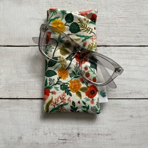 May include: A floral print glasses case with a pair of clear glasses on top of it. The case is made of fabric and has a white background with red, yellow, and green flowers.