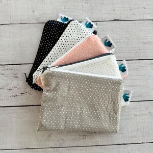 May include: A selection of small, zipped pouches in different colours and patterns. The pouches include black with white triangles, white with black triangles, pink with white dots, white with white dots, and grey with white hearts. Each pouch has a small tag with a blue elephant logo.