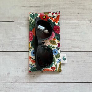 May include: Black sunglasses in a floral patterned case. The case has a small elephant logo on the side.