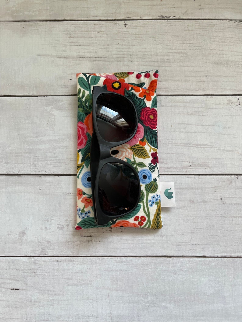 May include: Black sunglasses in a floral patterned case. The case has a small elephant logo on the side.
