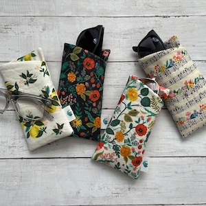 May include: Four different fabric eyeglass cases with floral patterns. The cases are all closed and feature a variety of floral designs, including lemons, flowers, and musical notes.