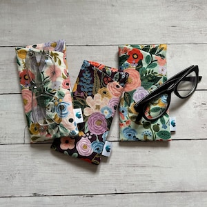 May include: Three floral patterned eyeglass cases with a pair of clear glasses and a pair of black glasses on a white wooden surface.
