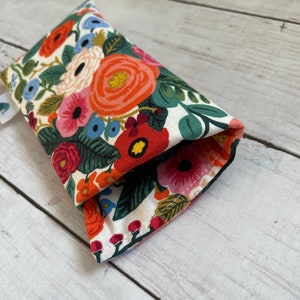 May include: A white fabric eyeglass case with a floral pattern featuring red, orange, pink, blue, and green flowers. The case is folded in half and the seam is visible.