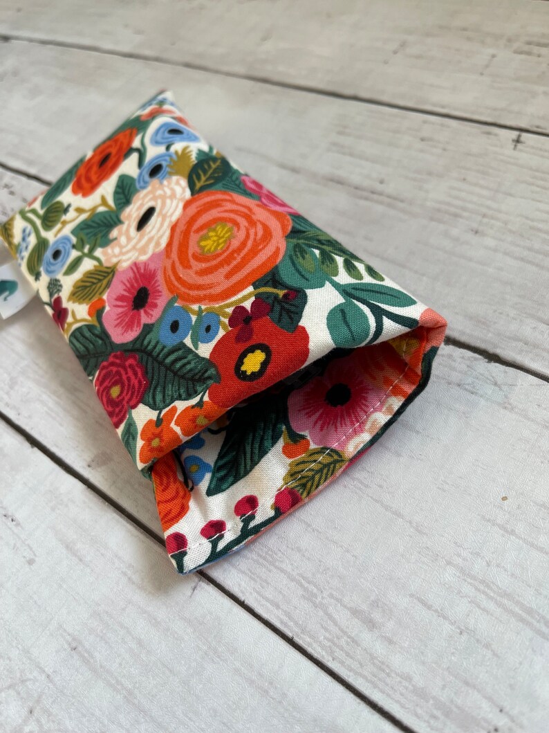 May include: A white fabric eyeglass case with a floral pattern featuring red, orange, pink, blue, and green flowers. The case is folded in half and the seam is visible.