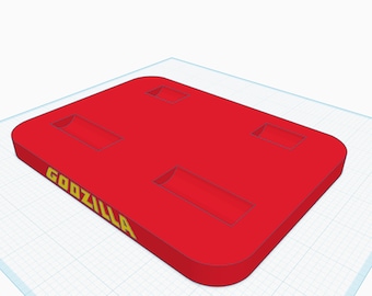 May include: Red plastic tray with four rectangular cutouts and the word "GOZILLA" printed in yellow letters.