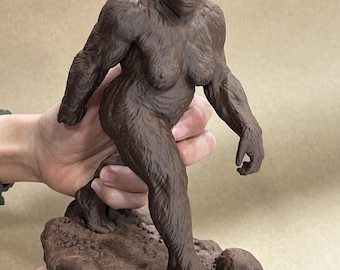 May include: A brown, textured figurine of a bipedal primate in a walking pose, standing on a rocky base. The figure features detailed fur patterns, defined musculature, and a forward-facing expression, captured in a solid, monochromatic dark brown finish.