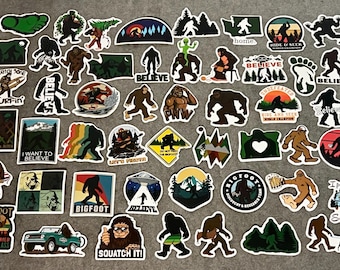 May include: A collection of numerous vinyl stickers featuring various illustrations of Bigfoot, including silhouettes, cartoon depictions, and scenic landscapes. The designs incorporate text such as Believe, Squatch It, and I party with Sasquatch.