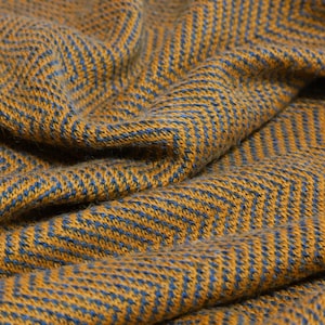 Könnte beinhalten: Ein Textilstoff mit einem gewebten Fischgrätenmuster in Senfgelb und Schieferblau. Das Material hat eine weiche, strukturierte Optik mit sichtbaren Falten und tiefen Knicken, die ein dynamisches Spiel von Licht und Schatten auf der Oberfläche erzeugen.