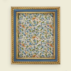 Puede incluir: Un marco de imagen azul y dorado con un fondo blanco y un patrón floral. El patrón presenta flores y hojas azules, verdes y naranjas.