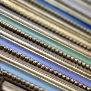 Op de afbeelding: Close-up van een verzameling fotolijsten met verschillende kleuren. De lijsten hebben een gouden rand met een kralenrand en geverfde secties in blauw, groen, paars en rood. De lijsten zijn schuin geplaatst, waardoor een gevoel van diepte ontstaat.