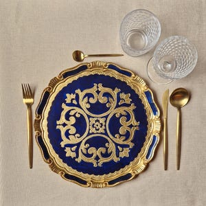 May include: A blue and gold charger plate with a decorative floral pattern. The plate has a scalloped edge and is perfect for adding a touch of elegance to any table setting.