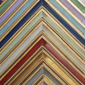 May include: Close-up of a collection of colourful picture frames. The frames are painted in various colours, including green, purple, blue, red, and gold. Each frame has a gold inner border with a beaded design. The frames are arranged in a zig-zag pattern.